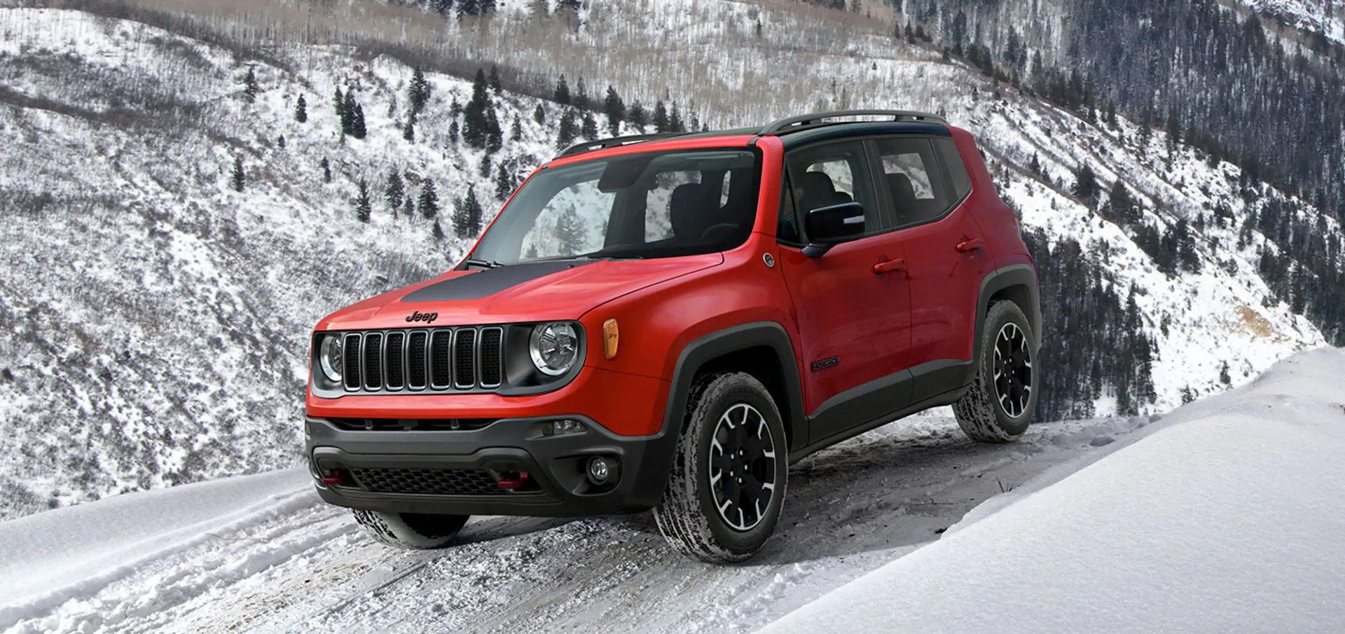 A red 2023 Jeep Renegade drives through the snow.